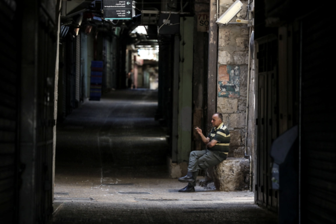 パレスチナ人の呼び掛けでゼネストが行われる中、エルサレム旧市街の市場にある休業した店の近くでたばこを吸う男性（ロイター）