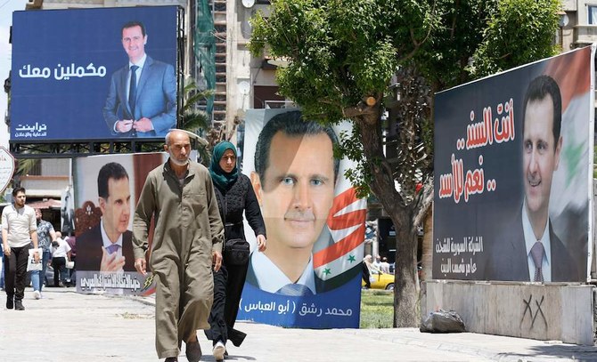 シリアのバッシャール・アサド大統領の選挙キャンペーン用看板の横を歩く人々。（AFP）