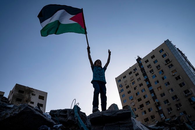 見物人の集まる中、パレスチナの国旗を掲げ歓声をあげる子供。2021 年 5 月 21 日、ガザ市アル・ジャラー ビルの瓦礫の横にて。(AP)