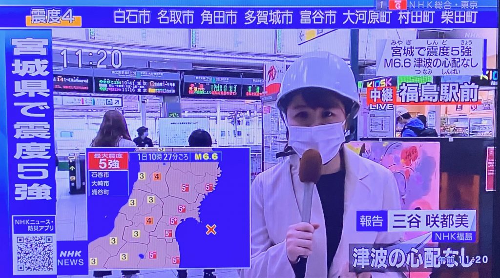 福島にあるJRの駅にいるヘルメットをかぶったNHKのレポーター。日本の北東部を今日の午前中に襲った強い地震のために運行が停止されている。（NHKの映像より