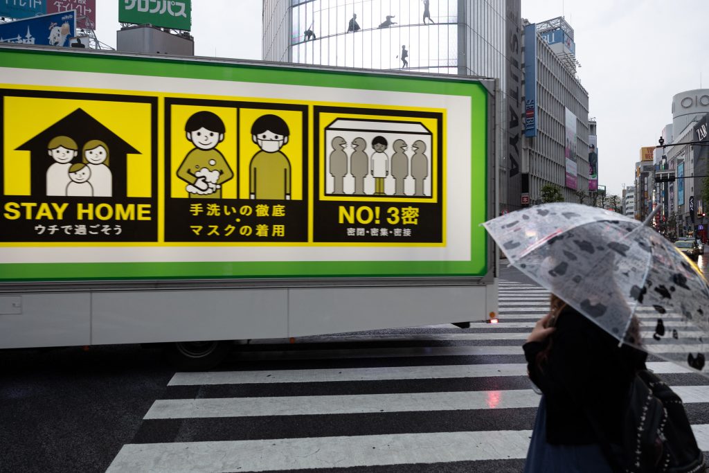 コロナウイルス予防対策のポスターが貼られたトラックが、緊急事態宣言下の東京渋谷の交差点を走っている。(AFP通信)