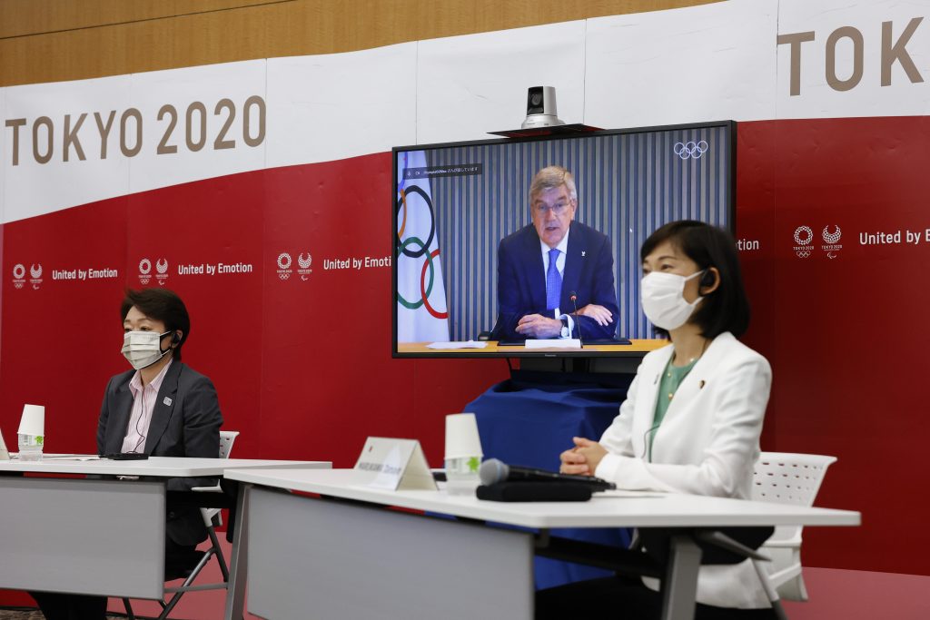 東京2020の橋本聖子会長(左)、日本の丸川珠代五輪相(右)、スクリーンに映るIOCのトーマス・バッハ会長は、東京の晴海アイランド・トリトンスクエアタワーYで行われた5者によるオンライン会議に出席した、2021年6月21日 (資料写真/AP)
