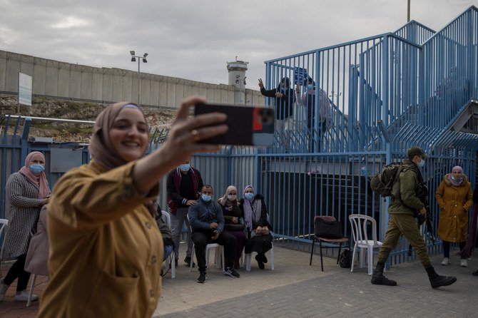 ヨルダン川西岸地区の都市ラマッラーとエルサレムの間のカランディア検問所で、イスラエルの医療チームから新型コロナワクチン接種を受けた後、自撮り写真を撮るパレスチナ人女性。 （ファイル写真：AP）