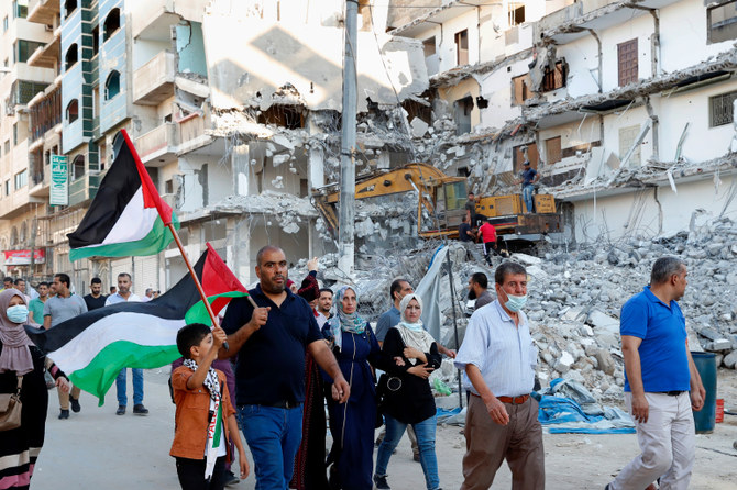 ガザ市でのデモで、イスラエルの空爆で破壊された建物の横を行進しながらパレスチナの旗を振る参加者たち。（AP通信写真）