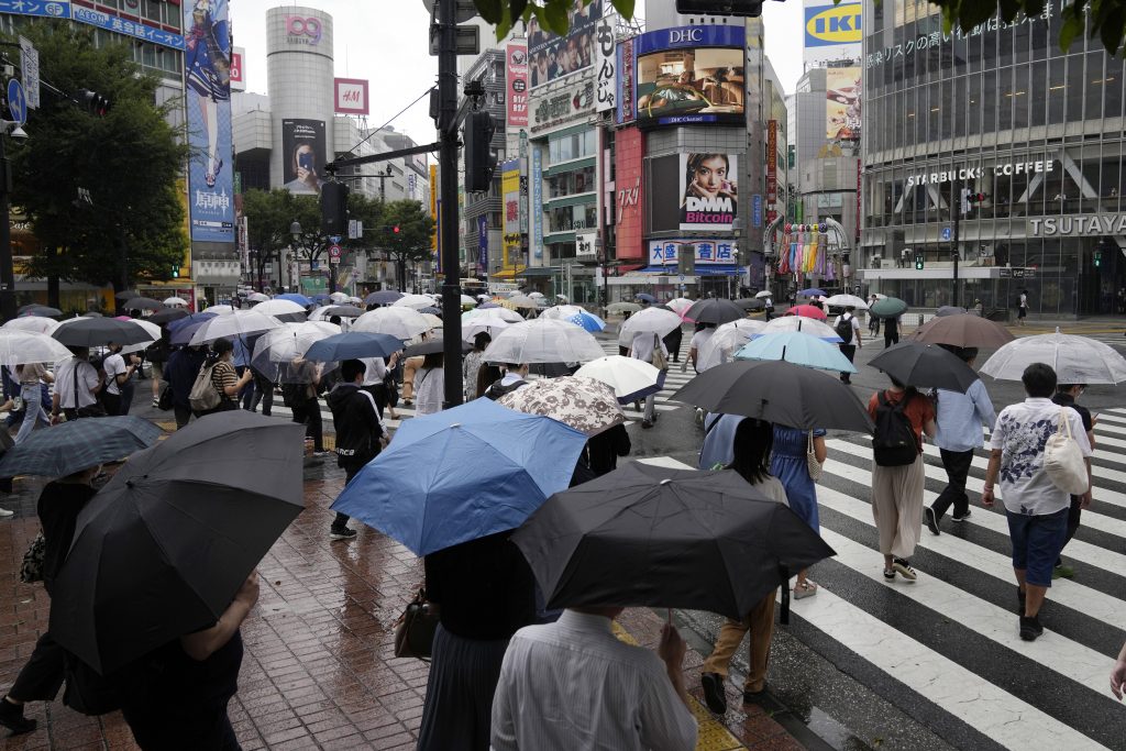 2021年7月27日、東京、横断歩道を覆う傘を持った朝の通勤者たち。（AFP通信）