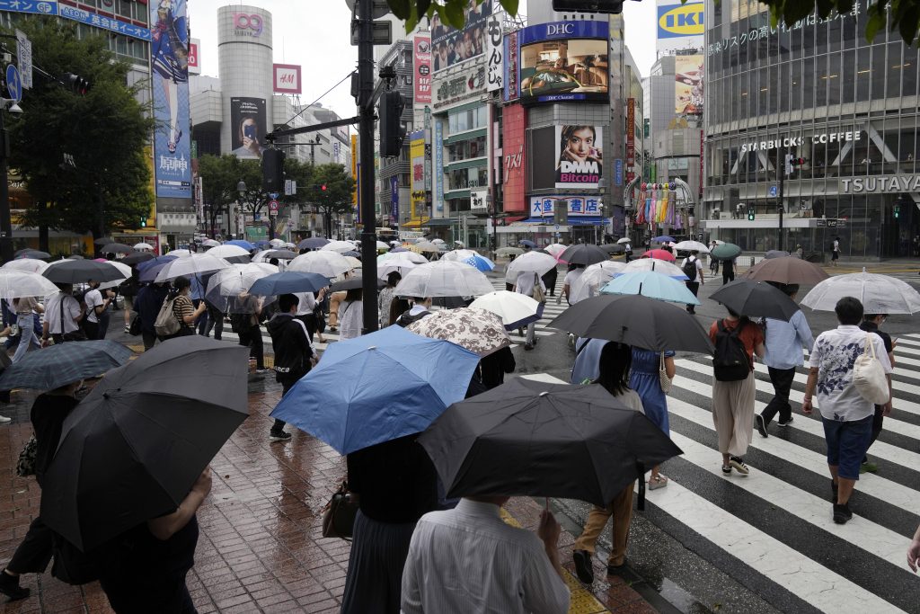 2021年7月27日、東京、横断歩道を覆う傘を持った朝の通勤者たち。(AFP通信)