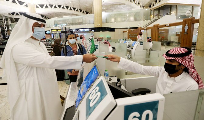サウジアラビアのリヤドにあるキング・ハーリド国際空港で、フェイスマスクを着用したサウジアラビア人男性が、サウジの出入国審査官からパスポートを受け取っている。（ロイター）