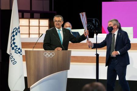 2021年7月21日に国際オリンピック委員会（IOC）が撮影して公開した、東京でのIOC総会の2日目の様子の写真。世界保健機関（WHO）のテドロス・アダノム事務局長（左）が、IOCのトーマス・バッハ会長からオリンピックの聖火のトーチを受け取っている。（AFP）