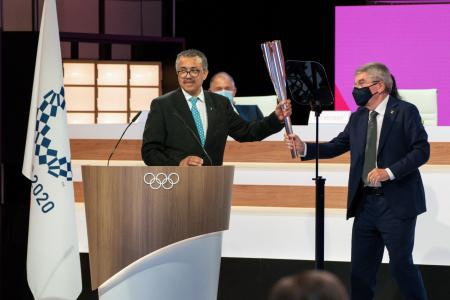 2021年7月21日に国際オリンピック委員会(IOC)が撮影して公開した、東京でのIOC総会の2日目の様子の写真。世界保健機関(WHO)のテドロス・アダノム事務局長(左)が、IOCのトーマス・バッハ会長からオリンピックの聖火のトーチを受け取っている。(AFP)