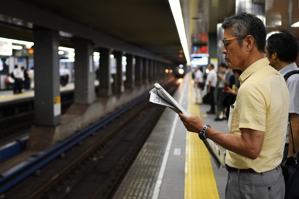大阪で電車を待ちながら新聞を読む男性。(AFP)