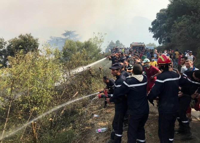アルジェリアのティジ・ウズ県のカビリー地方の山岳地帯で、ホースを使い森林火災の火を消そうとする消防隊員たちと村人たち。2021年8月13日。（ロイター）