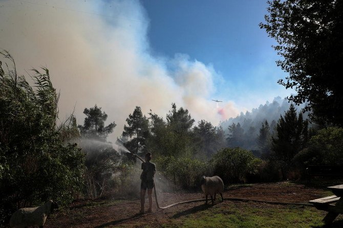 2021年8月15日、エルサレム郊外のショエバ村で、消防機と消防士が村に近づく前に山火事を消化しようとする中、庭に水を撒く女性。（ロイター通信）