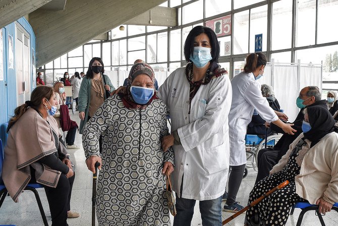 チュニジアの首都チュニスにあるエルメンザ・スポーツホールで、医療従事者が、ファイザー社/バイオンテック社の新型コロナウイルスワクチンの接種を受けに来た高齢女性を助けている。（AFP/資料写真）