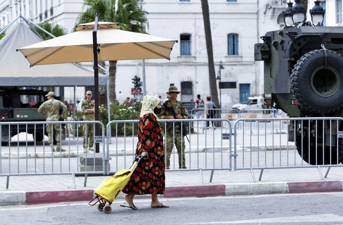2021年9月18日、首都チュニスで行われたカイス・サイード大統領に対する抗議デモで、警備に当たっているチュニジア軍兵士の前を女性が歩いている。(AFP)