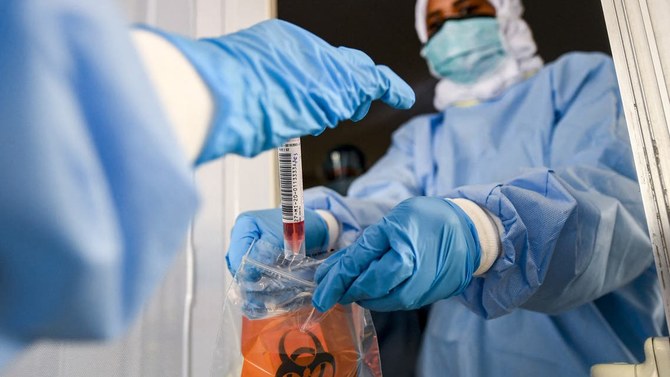アラブ首長国連邦、ドバイ首長国の湾岸地区al-Khawaneejの新型コロナウイルスドライブスルー検査センターで、研究室の職員たちが生体サンプルを袋に入れている。（ファイル写真：AFP）