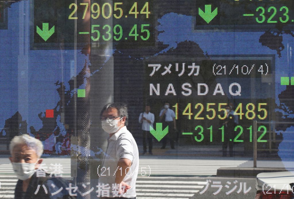 2021年10月5日、日本の東京の証券会社の外にある日本の日経平均株価と米国のナスダック指数を表示する電子掲示板に、新型コロナウイルス感染症(COVID-19)の流行の中で予防マスクを身に着ける人々が映っている。((資料写真/ロイター通信)