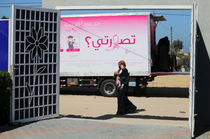 トラックに設置された移動式乳がん検診クリニックの前を歩いて通り過ぎる、子どもを連れたパレスチナ人女性。写真は2021年10月7日撮影。（ロイター通信）