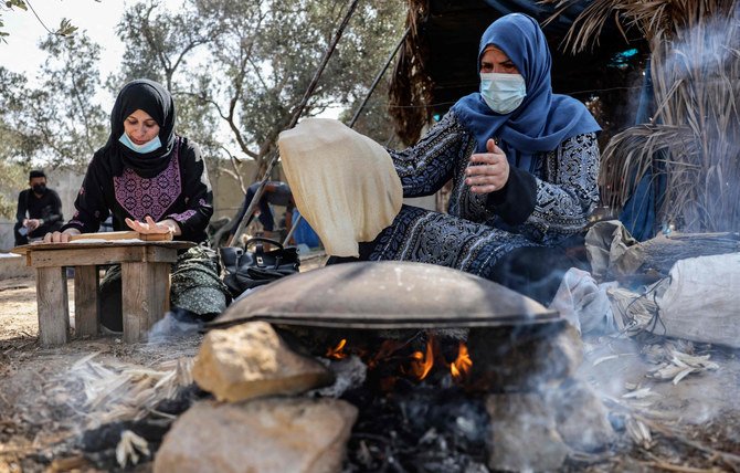 ガザ地区南部のハーンユーニスの野外でパンをこしらえる女性たち。（AFP）