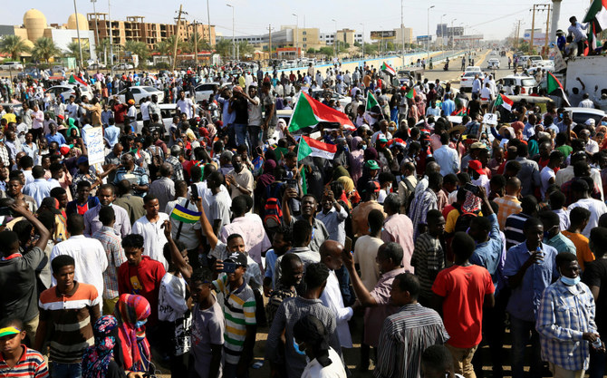  2021年10月21日、ハルツームで行われた軍事政権の復活を求める集会で、アブダッラー・ハムドゥーク首相の顔にバツ印が描かれたポスターの横を通り過ぎるスーダンのデモ参加者。（AFPファイル）