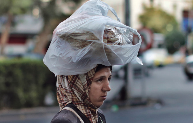 シリアの首都ダマスカスにて、パンを頭の上に乗せながら女性が通りを渡っている。(AP/写真）