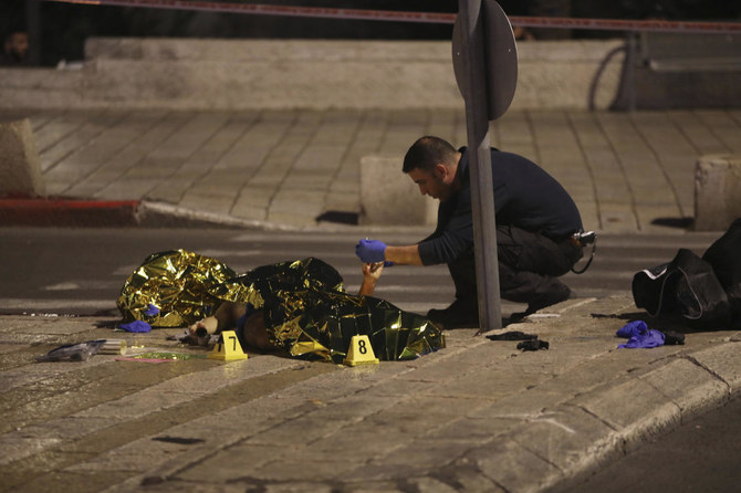 4日、エルサレム旧市街へ至るダマスカス門付近で撃たれた男の死体を調べているイスラエルの警察官。(AP)
