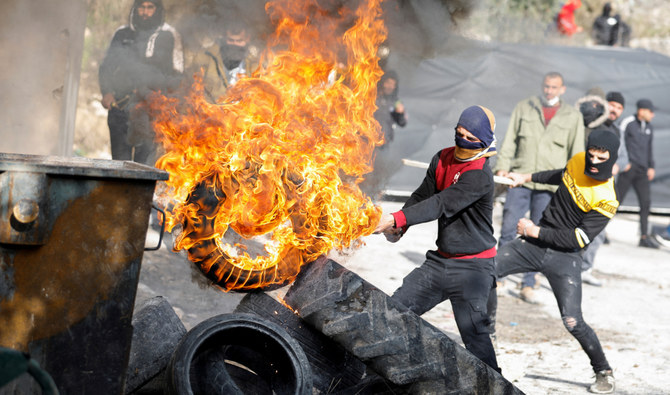2021年12月24日、イスラエルに占領されたヨルダン川西岸のブルカ村で、ユダヤ人入植者に対する抗議活動で燃えるタイヤを動かすパレスチナ人デモ隊。（ロイター）