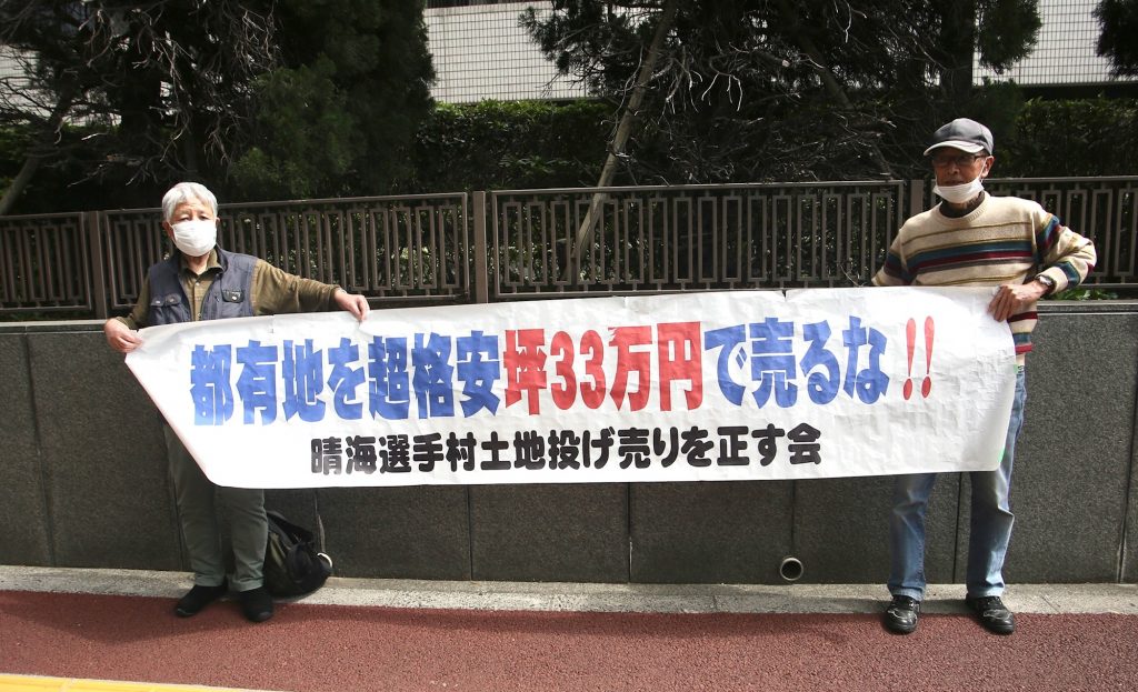 2021年4月1日、東京地裁前で横断幕を掲げる原告らの写真。五輪選手村土地売却をめぐり利益相反の疑いで訴訟。（ANJ/ピエール・ブティエ）