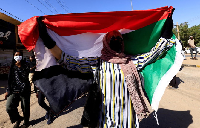 2022年1月6日、スーダンのハルツームで行われた軍事政権に反対する集会で、デモ隊が行進する中、スーダンの国旗を掲げる人。（ロイター）