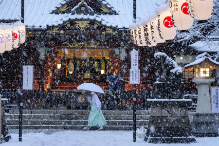2022年1月13日（木）東京で雪が降る中、巫女が本殿を通り過ぎ、作業員が階段を下りる。 （AP）
