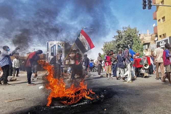 2022年1月9日ハルツームで、2021年10月の軍事クーデターに抗議する集会を行い、燃えたタイヤの横を歩くスーダンの抗議者ら。(AFP)