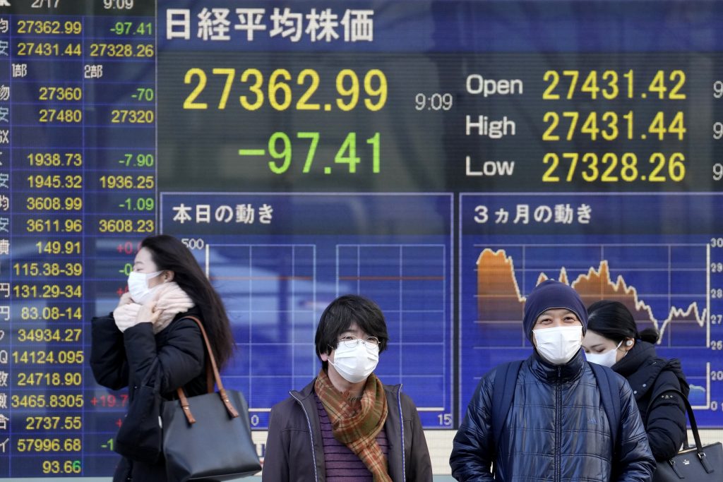 東京の証券会社前に設置された日経平均株価指数を示す電光掲示板の前を、マスクをした人々が通り過ぎている。2022年2月17日撮影（AFP通信）