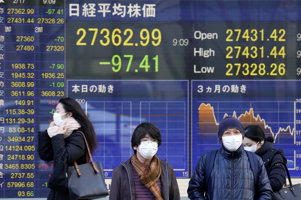 東京の証券会社前に設置された日経平均株価指数を示す電光掲示板の前を、マスクをした人々が通り過ぎている。2022年2月17日撮影(AFP通信)