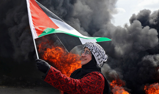 ヨルダン川西岸地区のブルカで、占領地での入植に反対する抗議行動中に燃えるタイヤの前で国旗を掲げるパレスチナの女性。（AFP通信/資料）