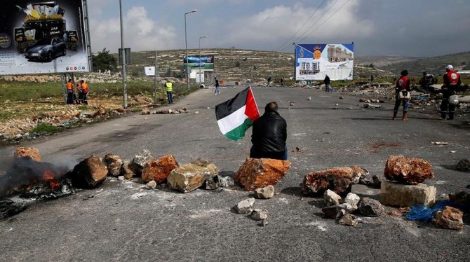 ラマッラー近郊のユダヤ人入植地、ベイト・エルでのイスラエル軍との衝突の中、1人の抗議活動者がパレスチナ旗を持って座っている。（ロイター通信）