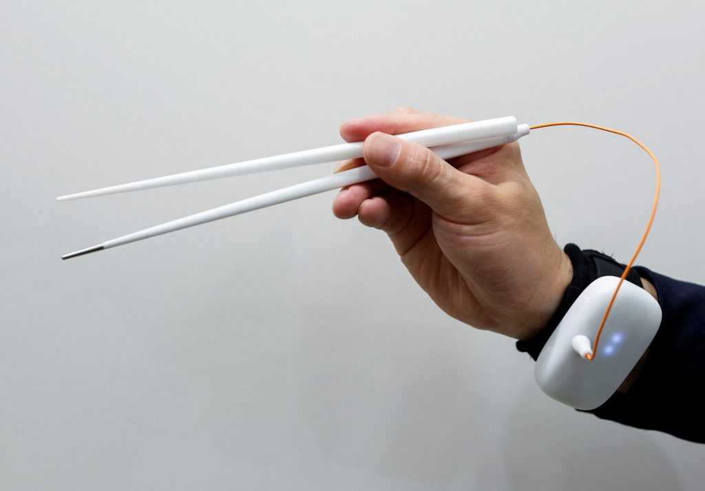 キリンホールディングスが明治大学理工学部の宮下芳明教授と共同開発した、電気刺激波形を用いて食べ物の味を強化することができる箸を実演する同社社員。2022年4月15日、東京にて。写真は2022年4月15日撮影。(ロイター/Issei Kato)