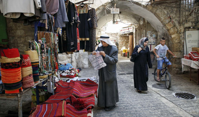 分断されたヨルダン川西岸地区のヘブロンの昔からの市場の路地にて、商品を閲覧するパレスチナ人男性と、そこに通り掛かった女性。（AFPファイル写真）
