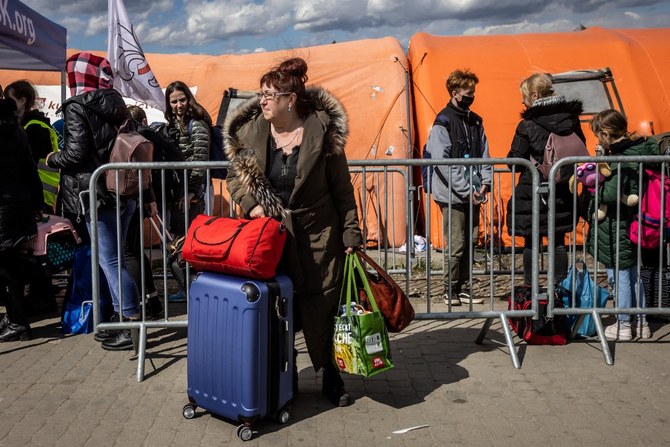 ポーランドのメディカにある国境検問所で、ウクライナとポーランドの間の国境を越えたウクライナ難民がバスを待つ中、スーツケースを持って立っている女性。（資料/AFP）