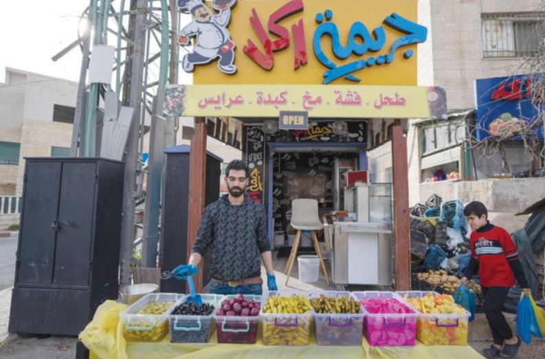 ヨルダン川西岸地区の都市ラマッラーで、アラビア語で「食品犯罪」と書かれた食堂の前で、さまざまなピクルスを陳列するパレスチナ人の販売員。（AP）
