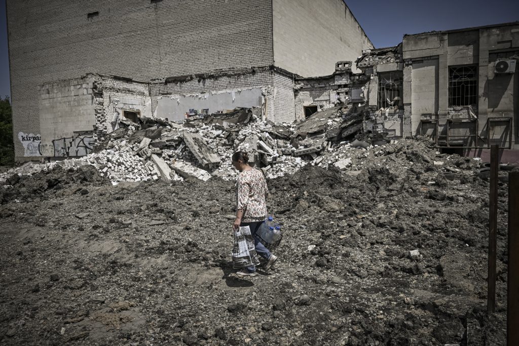 ロシアのウクライナ侵攻96日目の2022年5月30日、ウクライナ東部ドンバス地方のリシチャンシク市で、空爆により破壊された建物の前を歩く女性。（AFP通信）