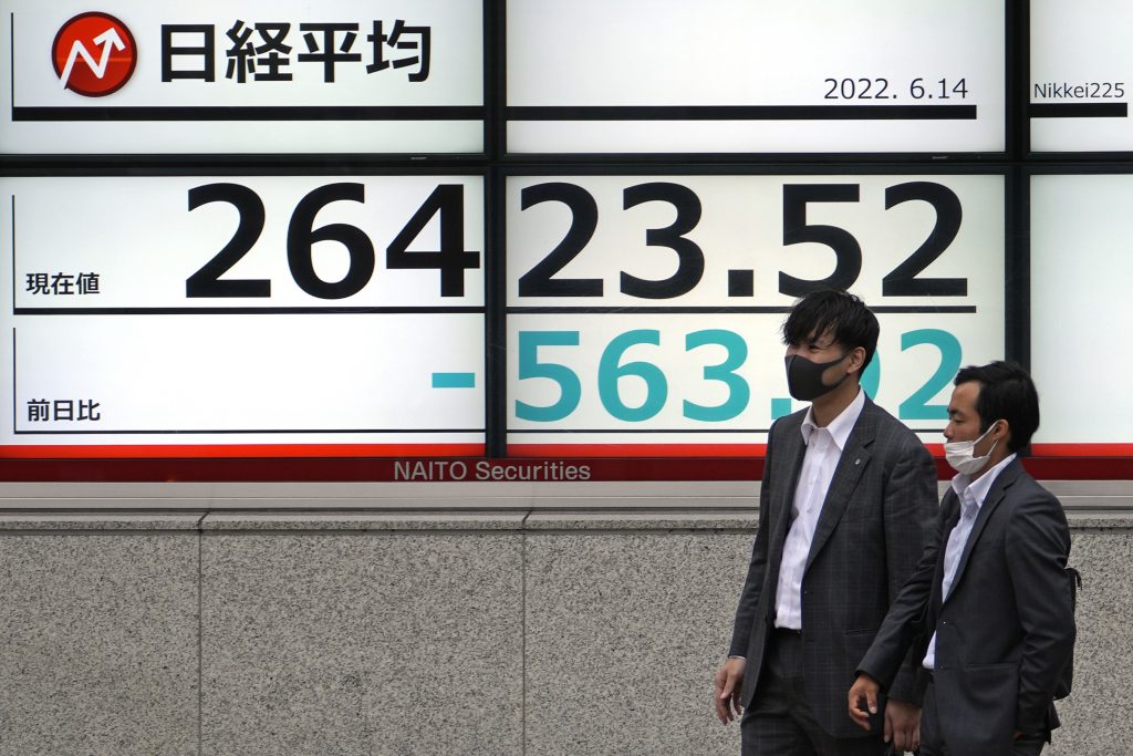 日経平均株価を表示する電光掲示板の前を通り過ぎるマスクを着けた人々。2022年6月14日、日本の東京。
