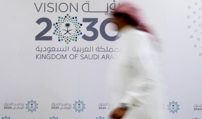 サウジアラビアのジェッダで行われた記者会見の後、「ビジョン2030」のロゴの前を歩くサウジアラビア人男性。（2016年6月7日）（ロイター）