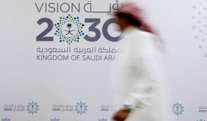 サウジアラビアのジェッダで行われた記者会見の後、「ビジョン2030」のロゴの前を歩くサウジアラビア人男性。(2016年6月7日)(ロイター)
