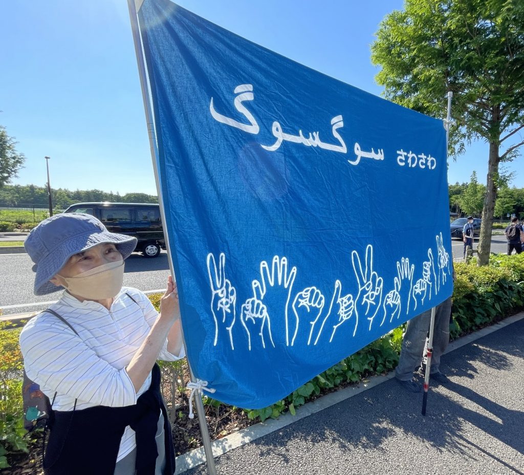アラビア語で「一緒に」という意味の「サワサワ」という歓迎の言葉が書（アラビア語で「一緒に」という意味の「サワサワ」という歓迎の言葉が書かれた横断幕を掲げる日本の支援者たち。（ANJP写真）