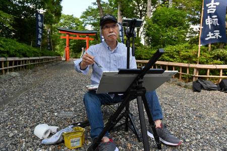 2022年5月25日撮影。千葉県いすみ市の神社で携帯電話を使って動画を撮影しながら水彩画を描く日本人アート講師の柴崎春通さん。(AFP)