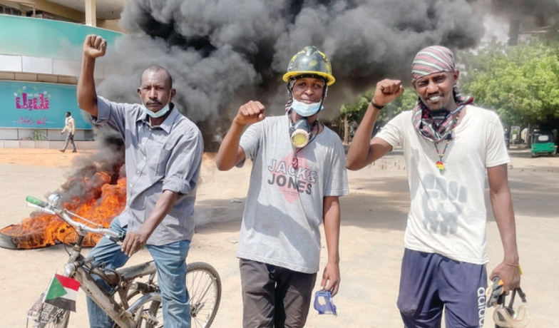 軍事政権に反対するデモにて、燃えるタイヤの前でジェスチャーをする抗議者ら＝スーダン・ハルツーム（ロイター/File）