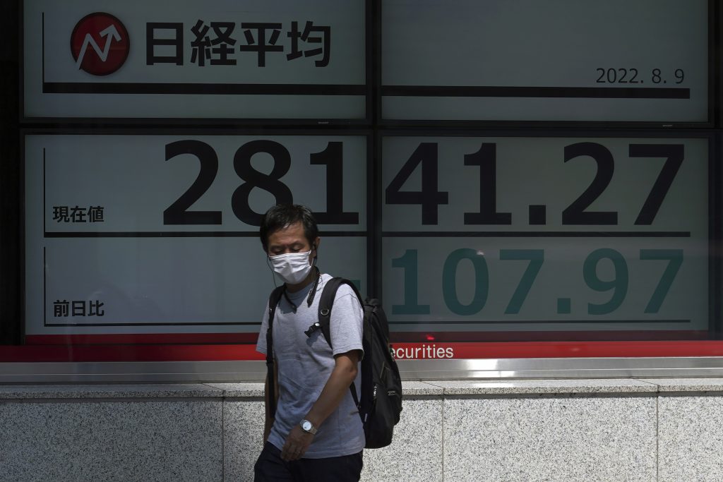 東京の証券会社の電子株価ボードが日経225指数を表示する前を、マスクを着けて歩く人。2022年8月9日撮影。（資料写真/AP）