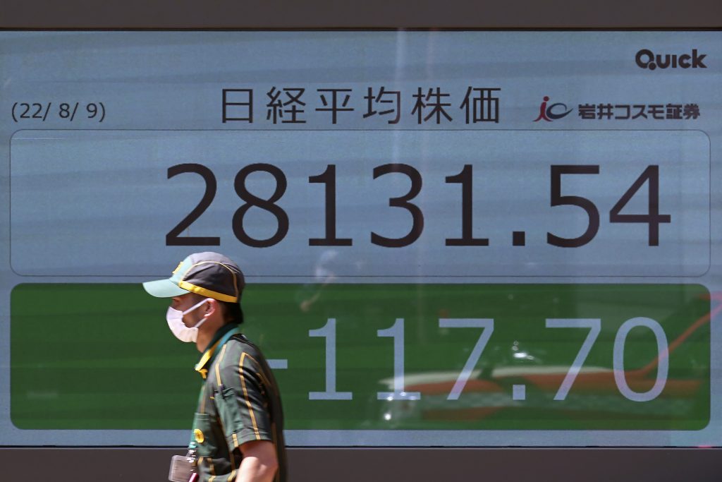 2022年8月9日、東京の証券会社で、日本の日経平均株価を表示する電光掲示板の前を歩く防護マスク姿の人物。(ファイル写真/AP)
