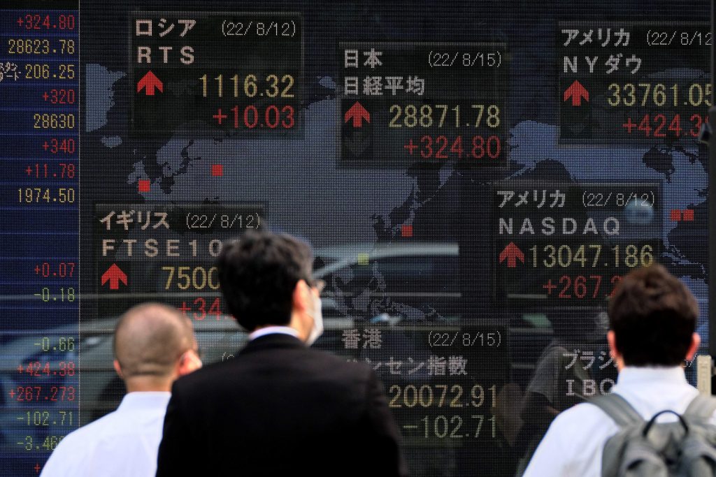 東京証券取引所（トップC）の終値など世界の株式市場の数字を表示する電光掲示板の前を歩く人々。2022年8月15日、東京。（AFP）
