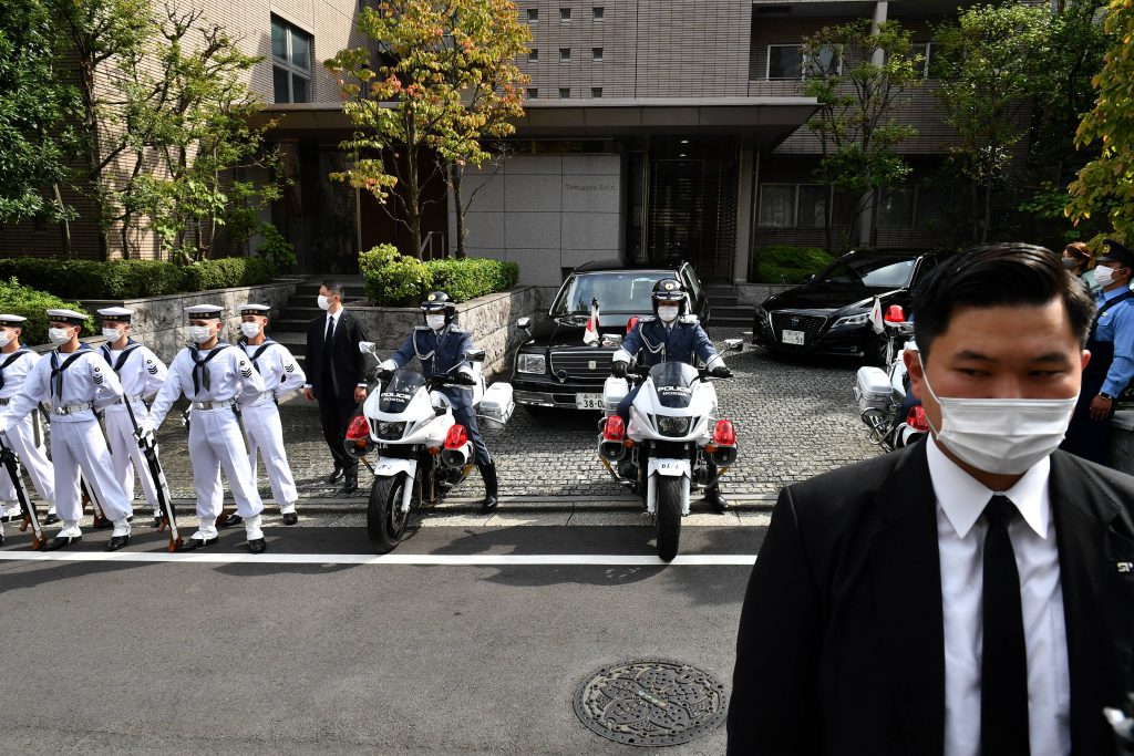 日本の安倍晋三元首相の私邸の外で直立不動の姿勢で立つ儀仗隊員（左）。この後、国葬のために遺骨が日本武道館に運ばれた。2022年9月27日、東京。（AFP）