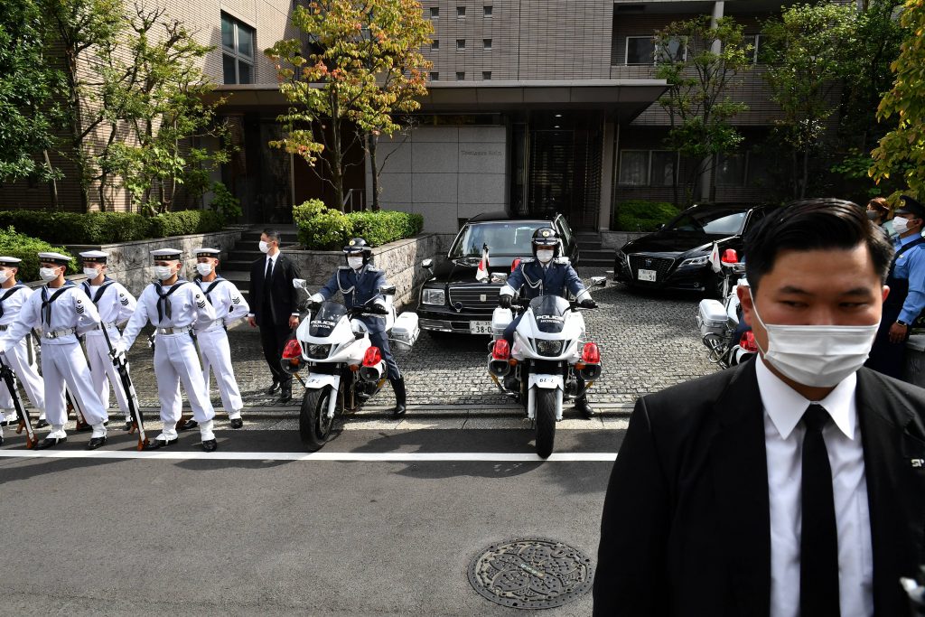 日本の安倍晋三元首相の私邸の外で直立不動の姿勢で立つ儀仗隊員(左)。この後、国葬のために遺骨が日本武道館に運ばれた。2022年9月27日、東京。(AFP)
